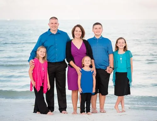 Family of five standing together on a beach with ocean waves in the background