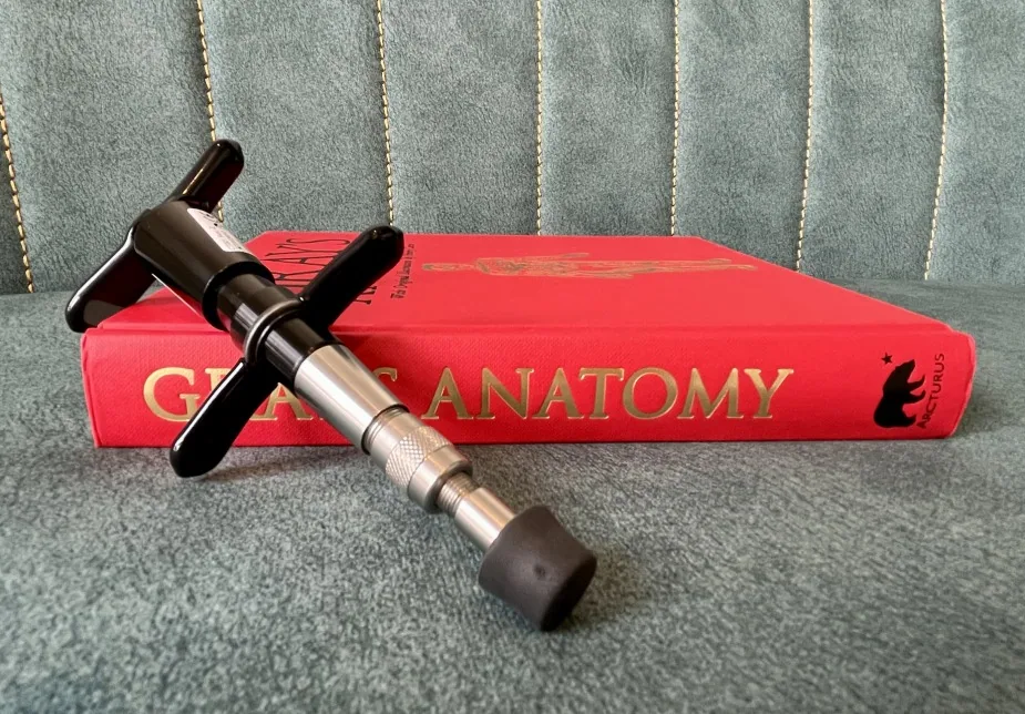 Chiropractic adjustment tool resting on a red anatomy textbook against a gray quilted surface